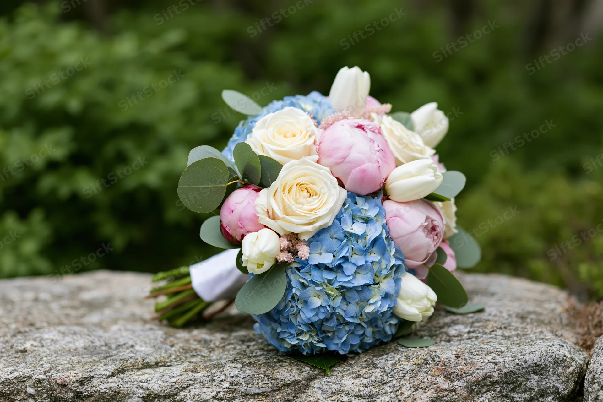 Bridal bouquet with roses, hydrangea, peonies and tulips resting on a rough stone outdoors