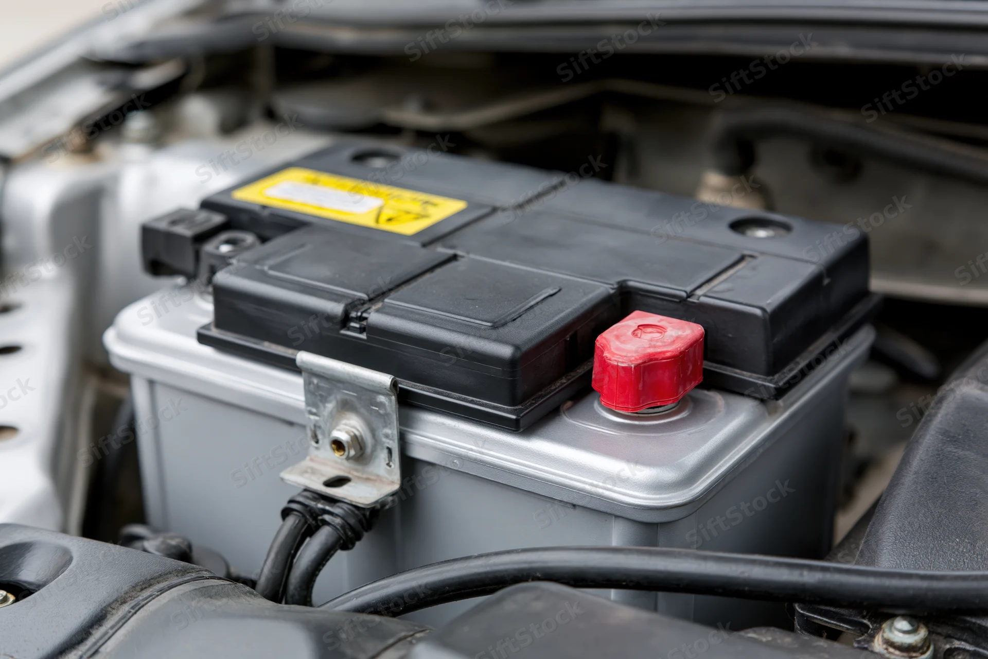 Car battery secured in open engine bay with red and black terminals and cables connected