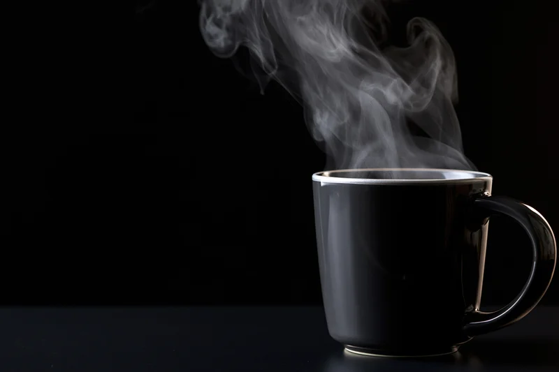 Black ceramic coffee mug with rising steam on dark surface