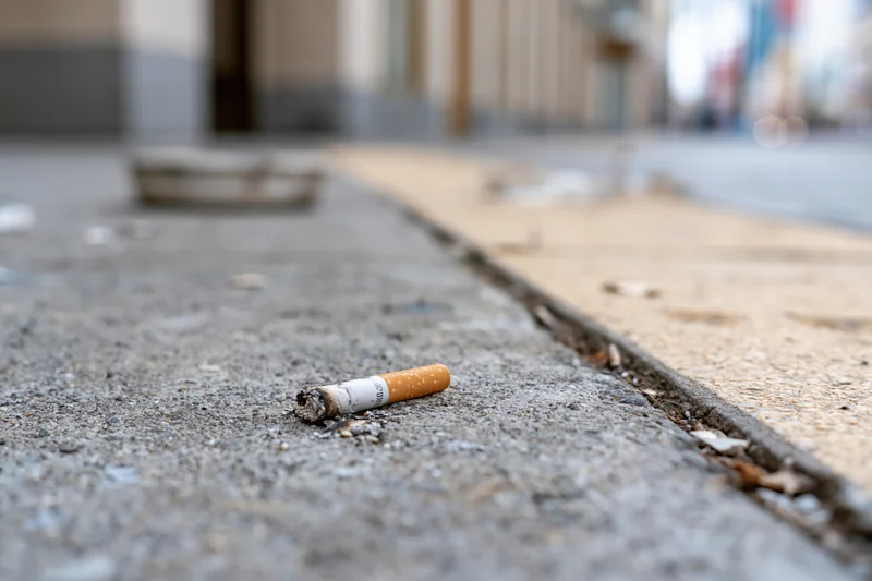 Cigarette butt lying on a concrete sidewalk in an urban setting