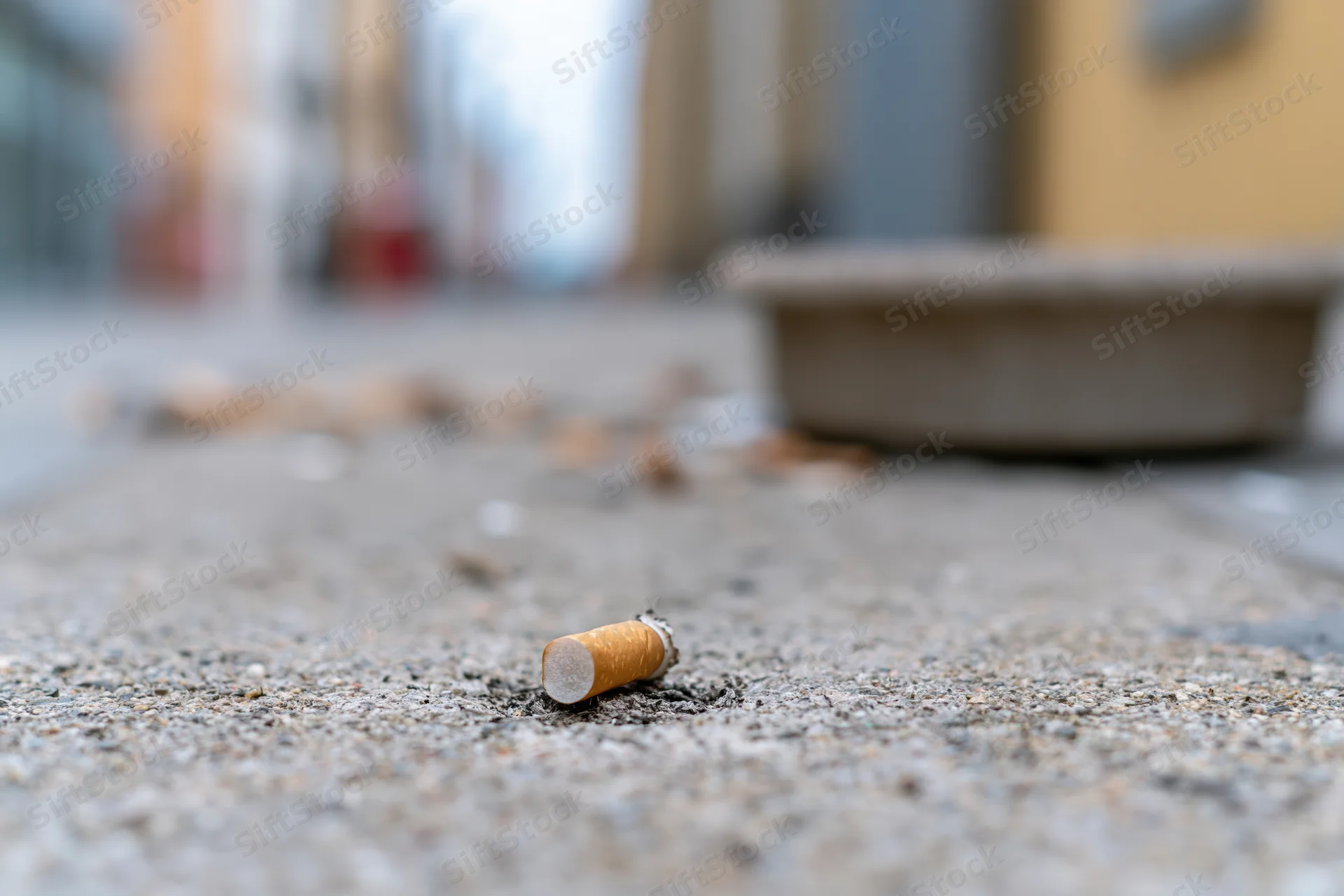 Cigarette butt lying on a concrete sidewalk with scattered debris in the background