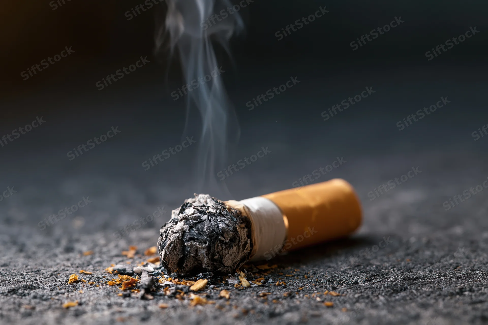 Cigarette butt with smoke rising on dark concrete floor