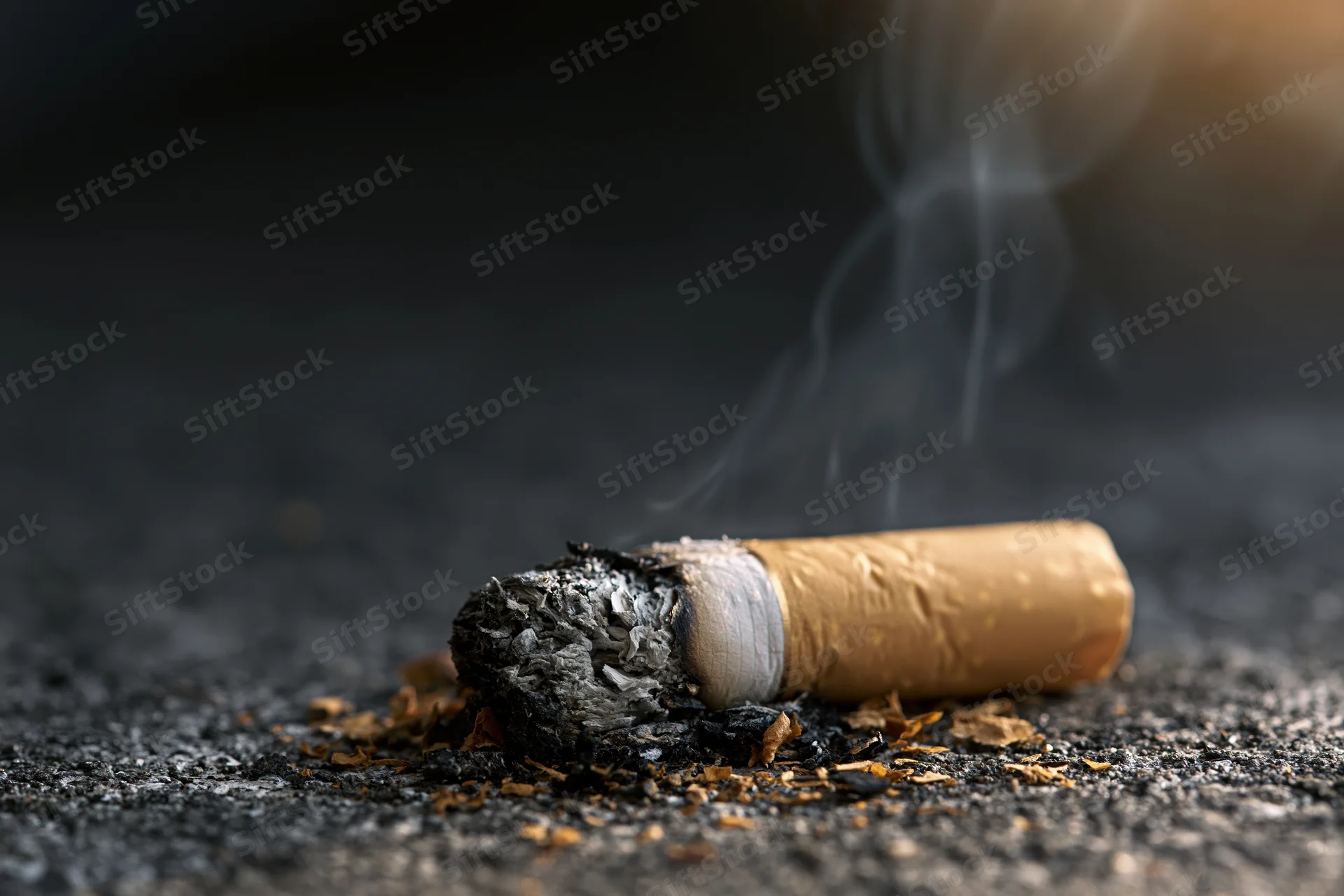 Cigarette butt with smoke rising on dark concrete floor