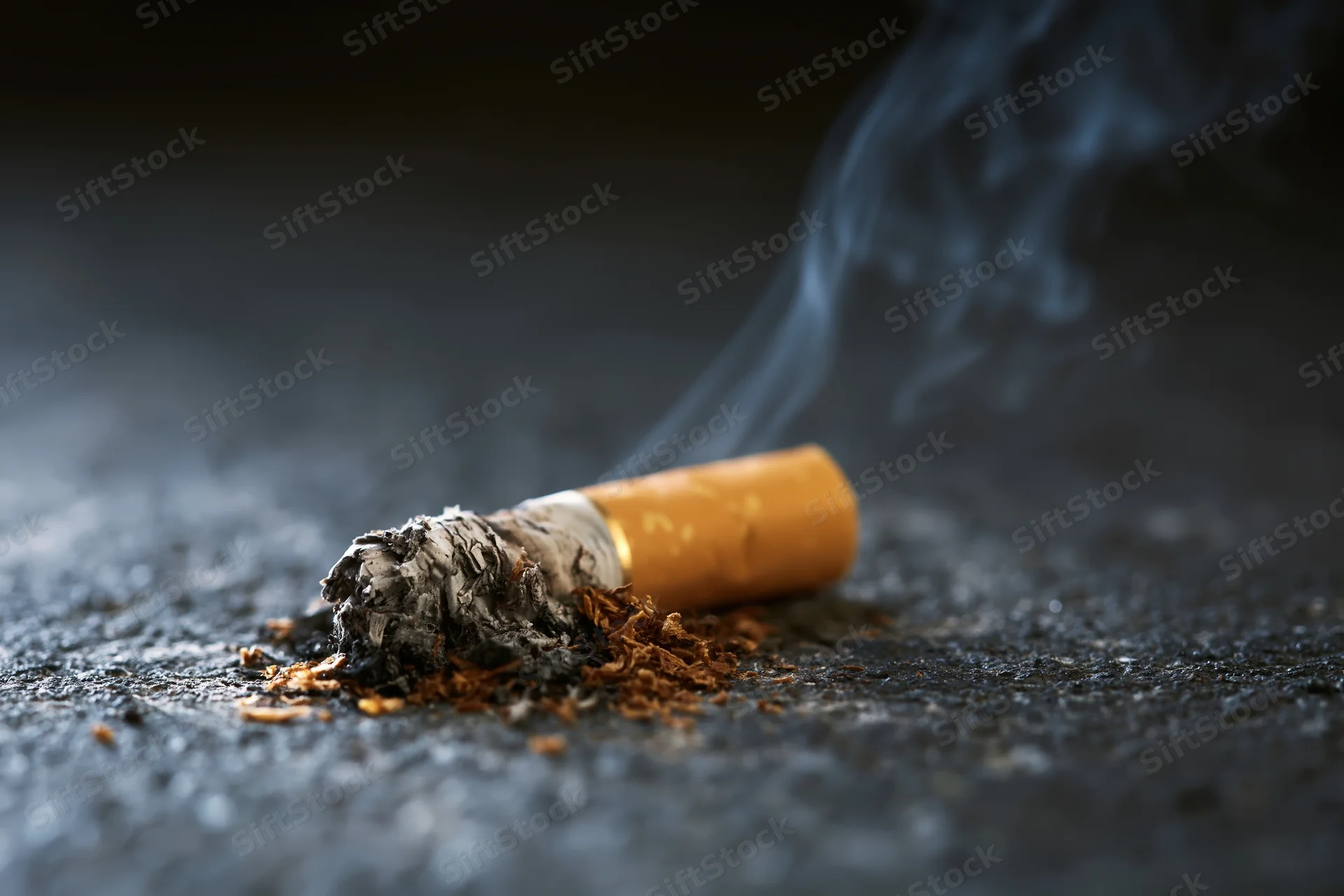 Cigarette butt with smoke rising on dark concrete floor