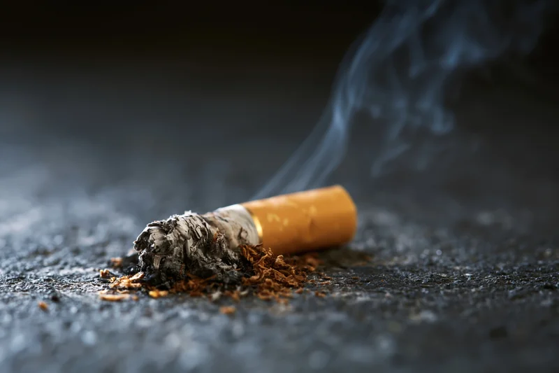 Cigarette butt with smoke rising on dark concrete floor