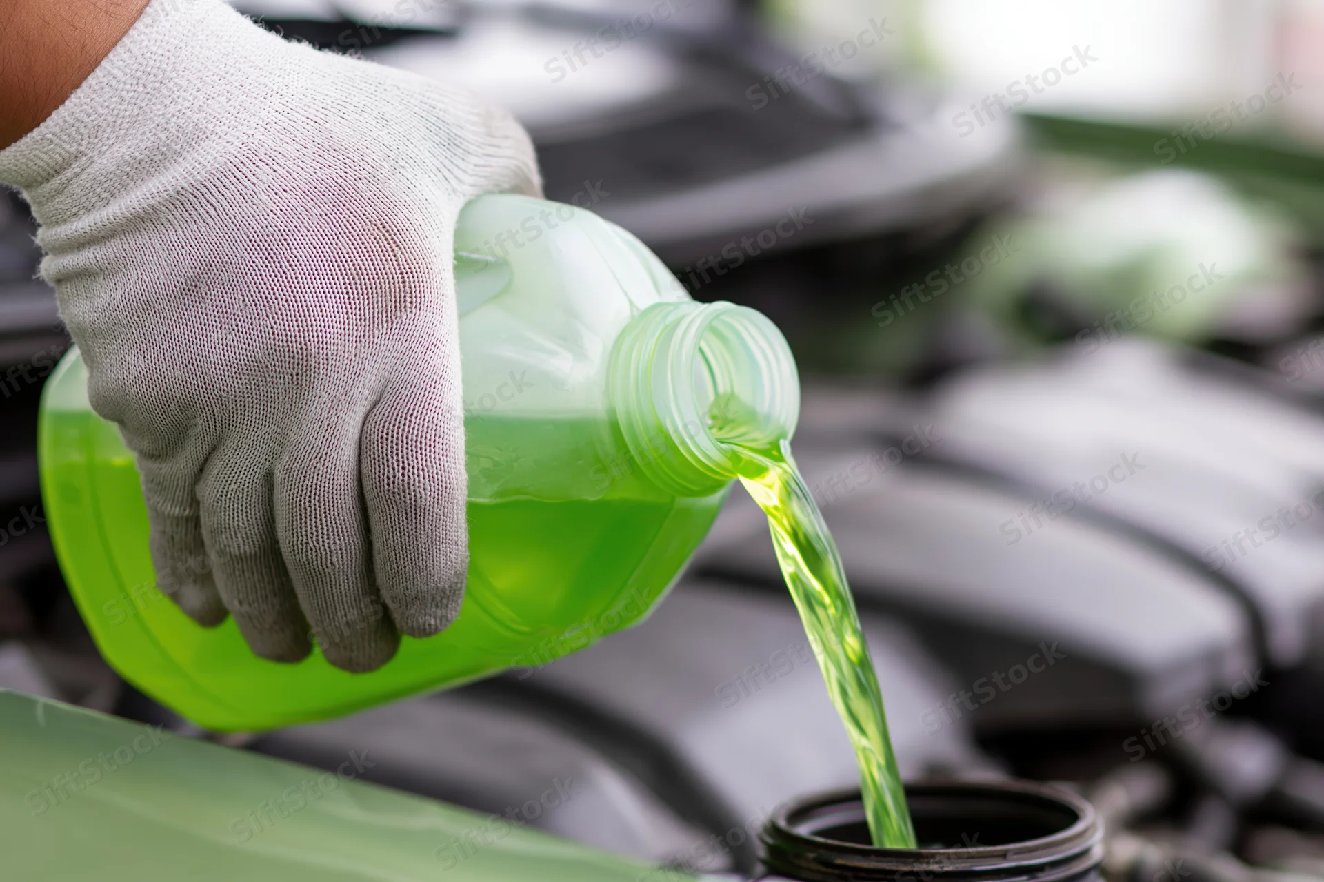 Gloved hand pouring green coolant into car engine reservoir