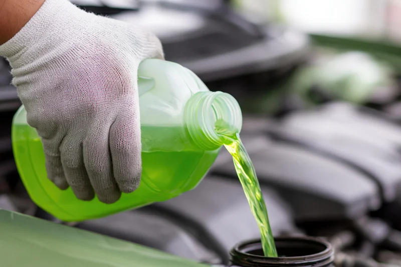 Gloved hand pouring green coolant into car engine reservoir
