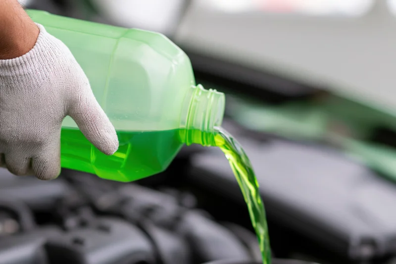 Gloved hand pouring green coolant into car engine bay