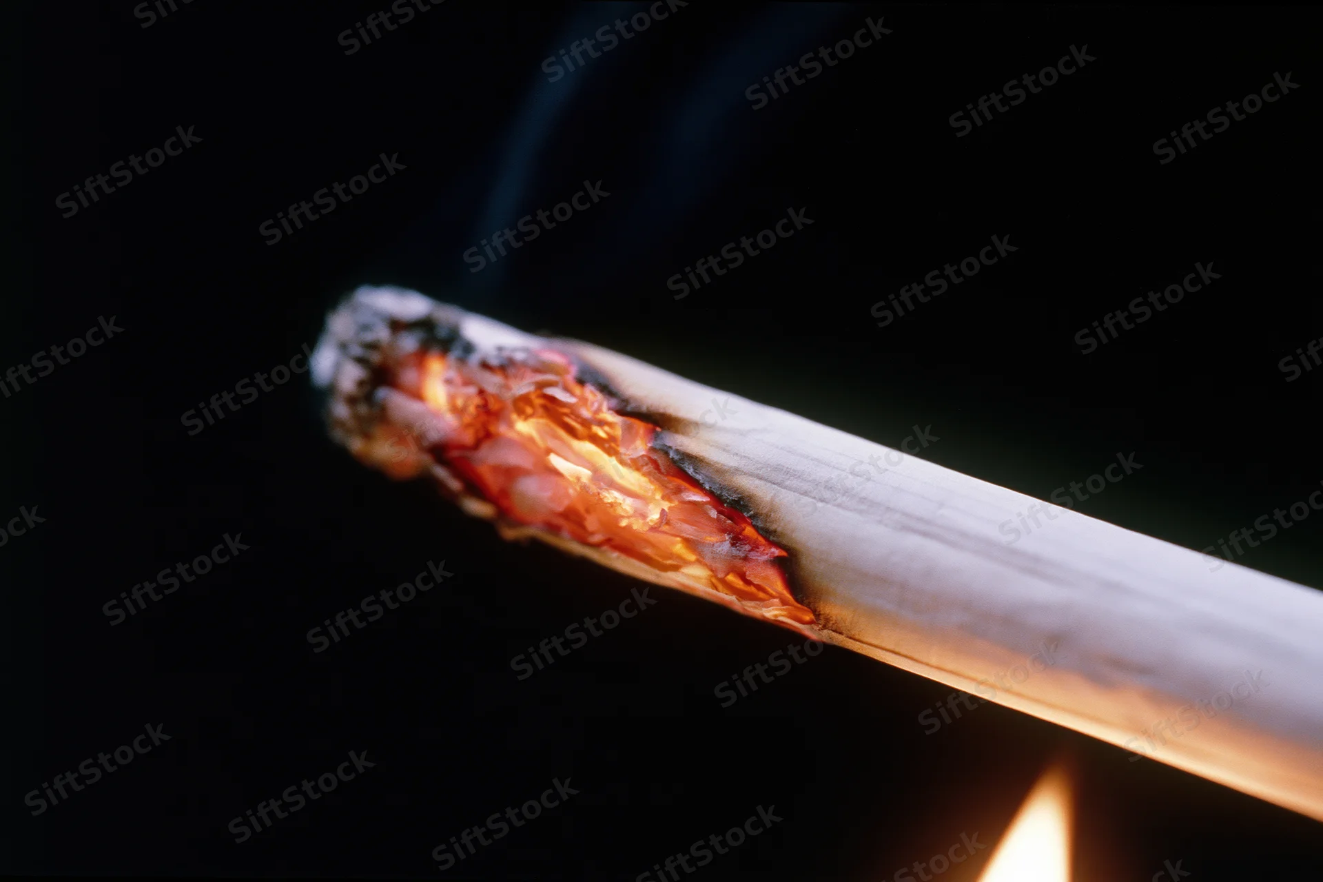 Lit cigarette burning with glowing ember and smoke against dark background
