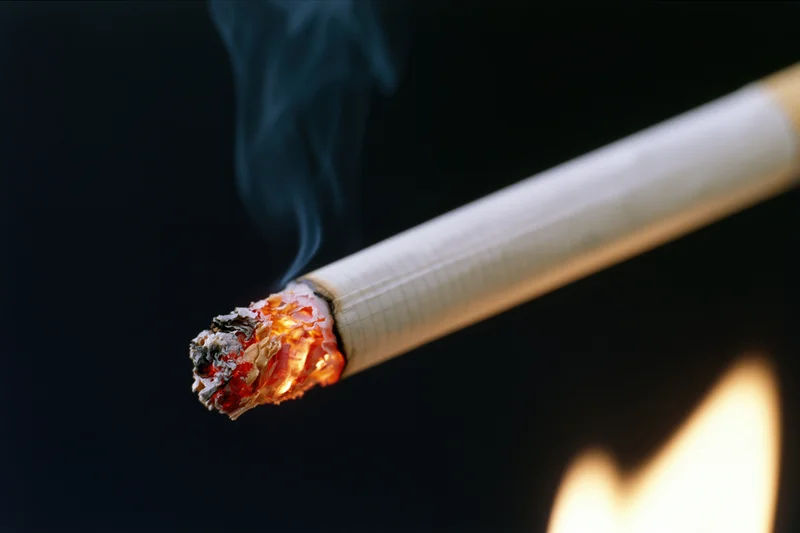 Lit cigarette burning diagonally with smoke and flame against dark background