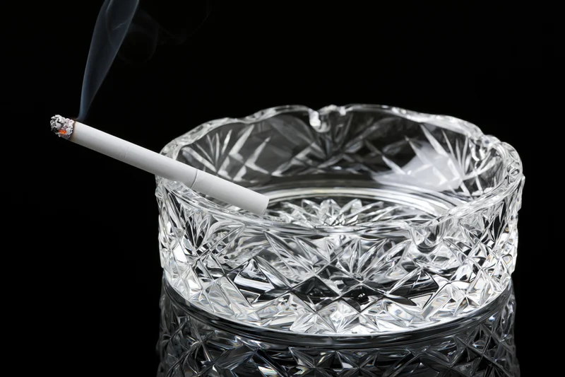 Lit cigarette resting in a heavy cut-crystal glass ashtray against black background