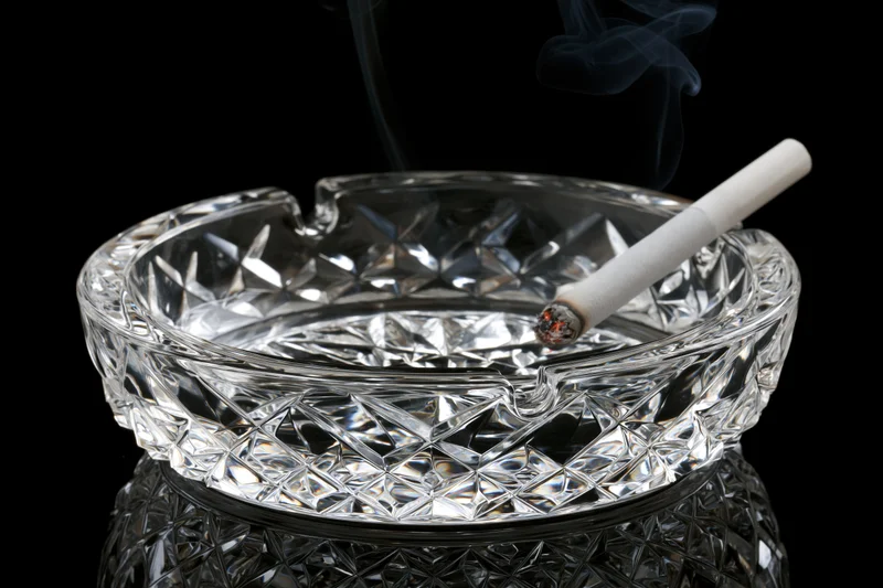 Lit cigarette resting in a heavy cut-crystal glass ashtray on black background