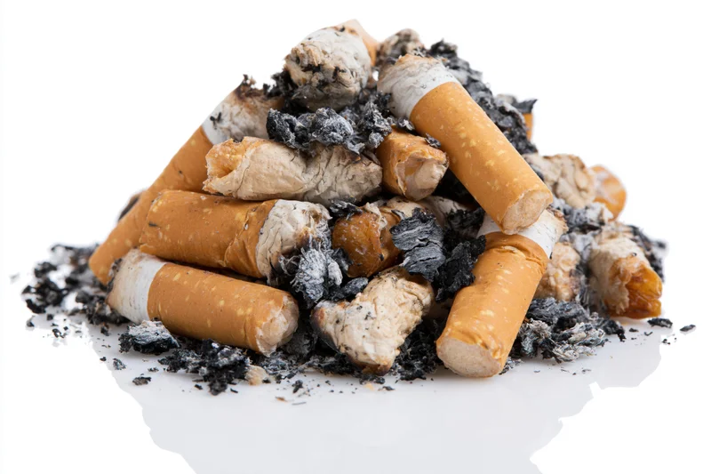 Pile of used cigarette butts with ash and tobacco residue on white background