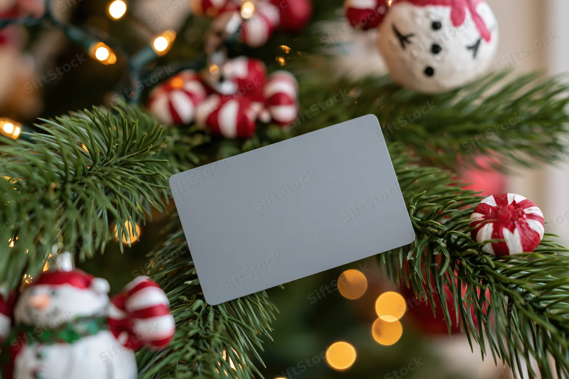 Plain matte gray credit card resting on decorated christmas tree branches with ornaments and lights