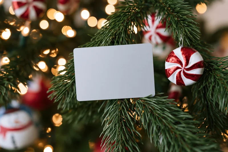 Plain gray card resting on a decorated christmas tree branch with ornaments and lights