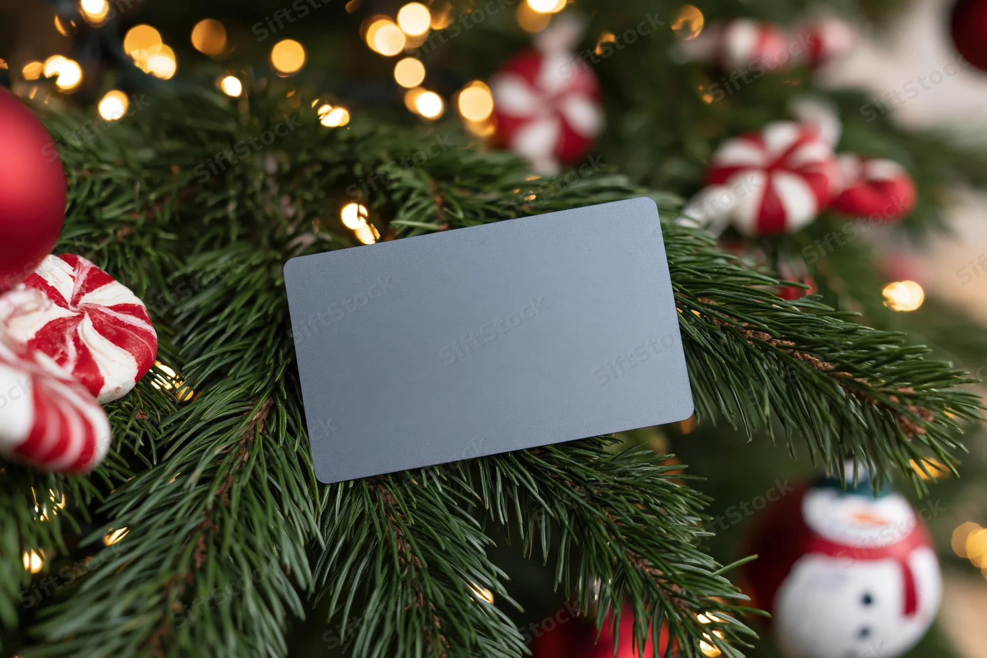 Matte gray credit card resting on decorated christmas tree branch with ornaments and lights