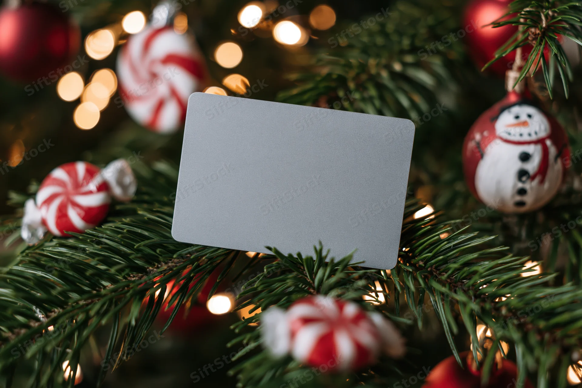 Plain gray credit card resting on decorated christmas tree branch with ornaments and lights