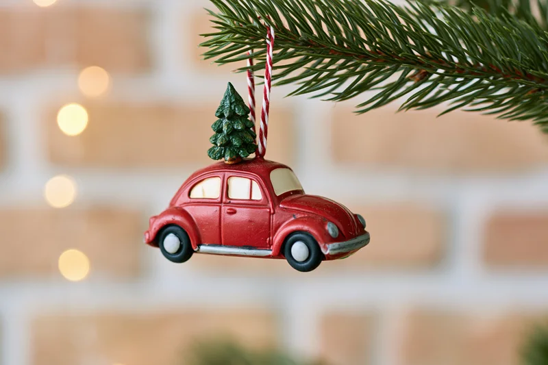 Red vintage car ornament with miniature tree on roof hanging from pine branch