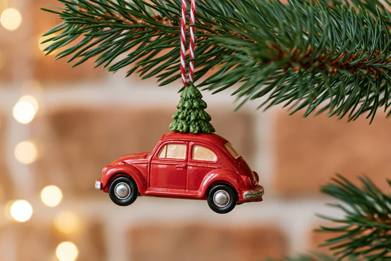 Red vintage car ornament with miniature tree on roof hanging from pine branch