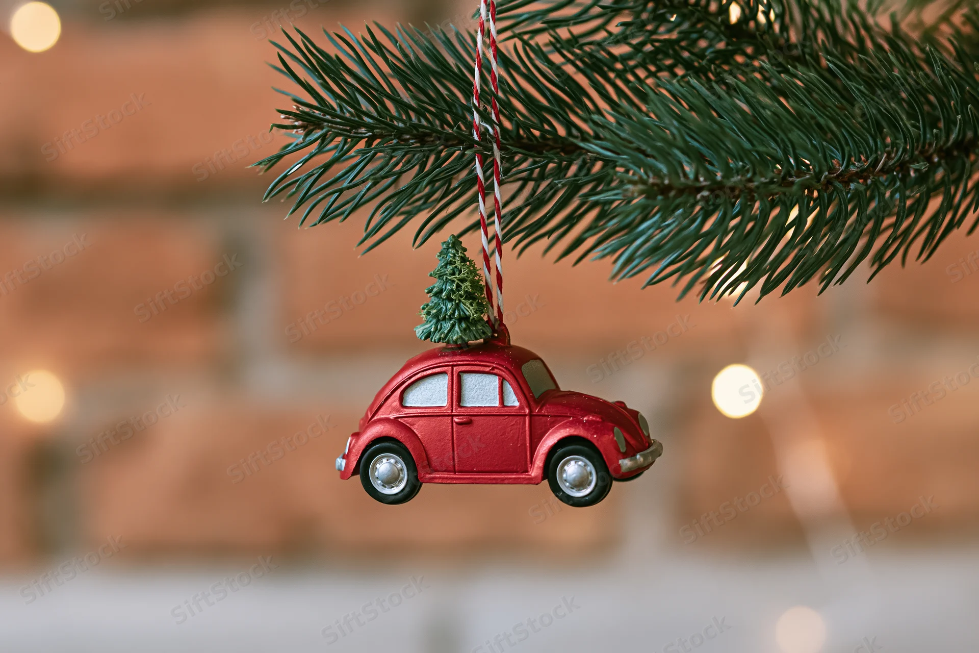 Red vintage car ornament with miniature tree on roof hanging from pine branch