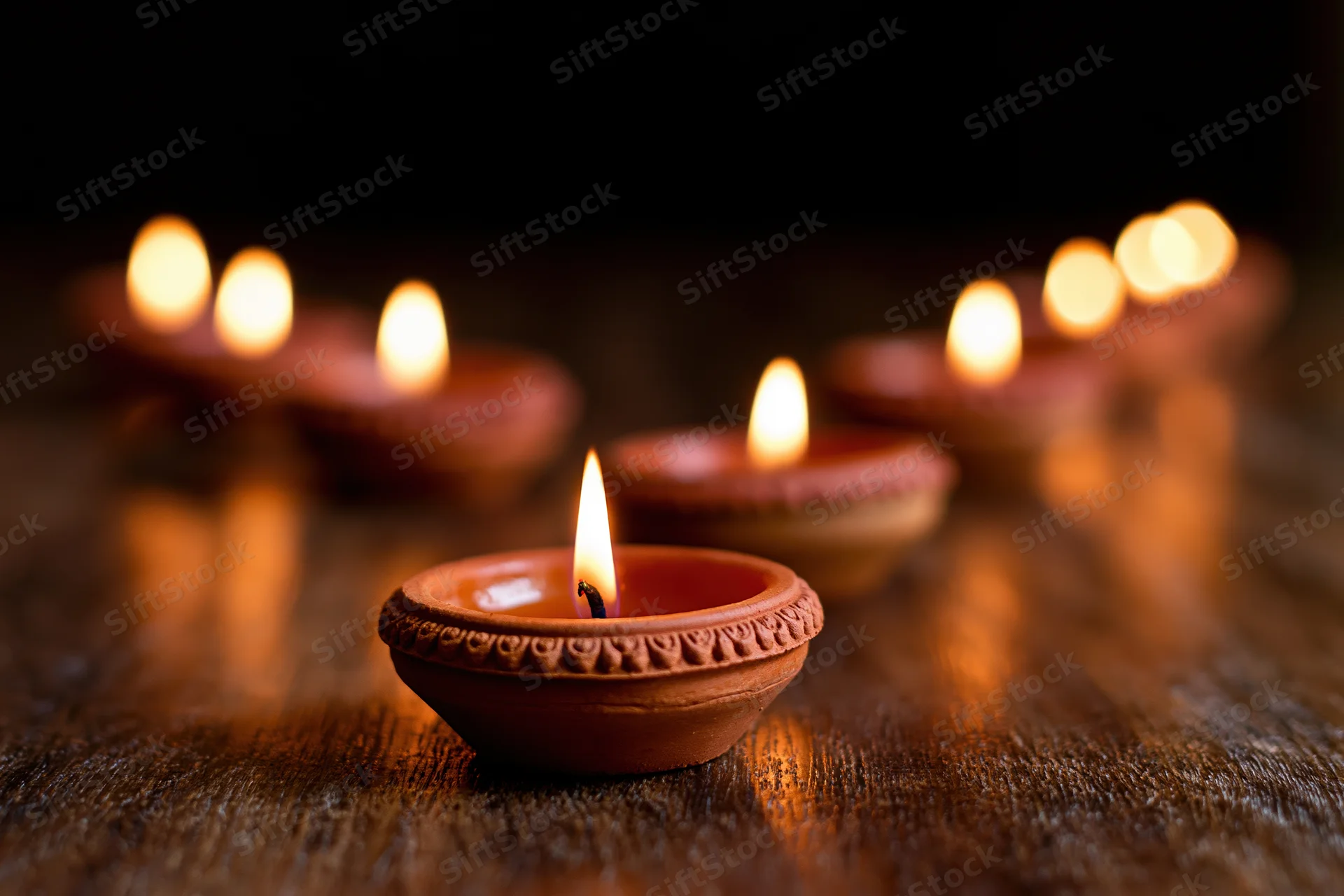 Lit clay diya oil lamps arranged in diagonal line on wooden surface