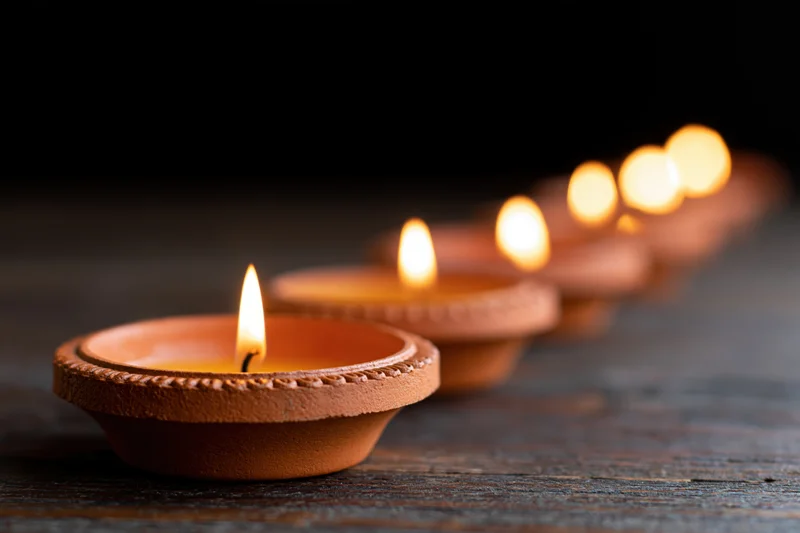 Row of lit clay diya oil lamps arranged diagonally on wooden surface