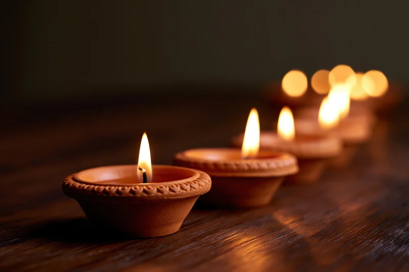 Row of lit clay diya oil lamps arranged diagonally on wooden surface
