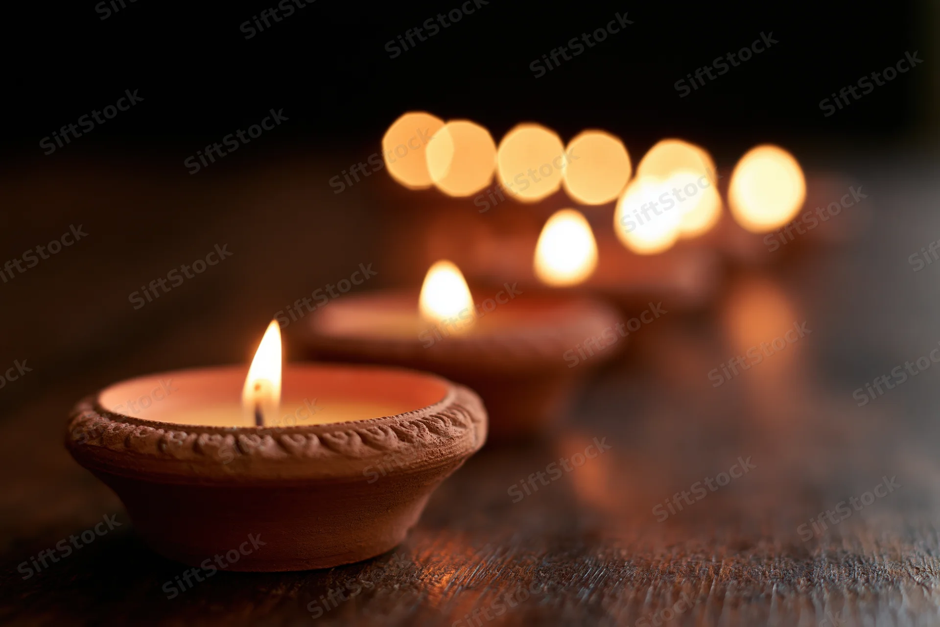 Lit clay diya oil lamps arranged in diagonal row on wooden surface