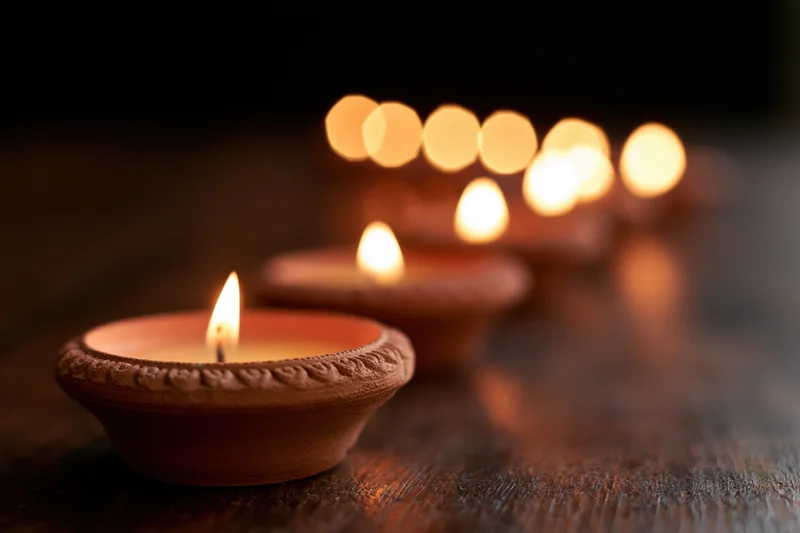 Lit clay diya oil lamps arranged in diagonal row on wooden surface