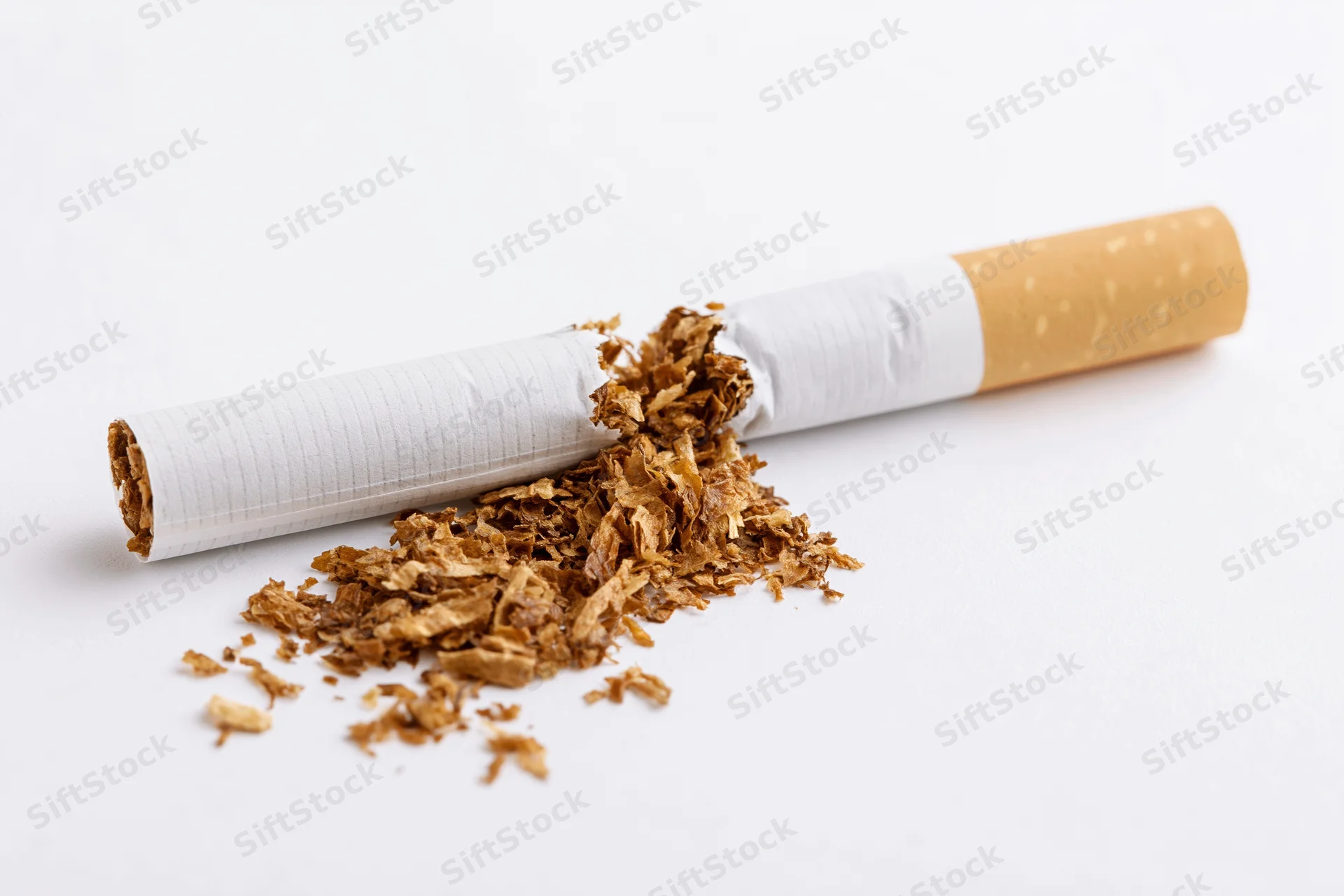 Broken cigarette snapped in half with loose tobacco spilling out on white surface