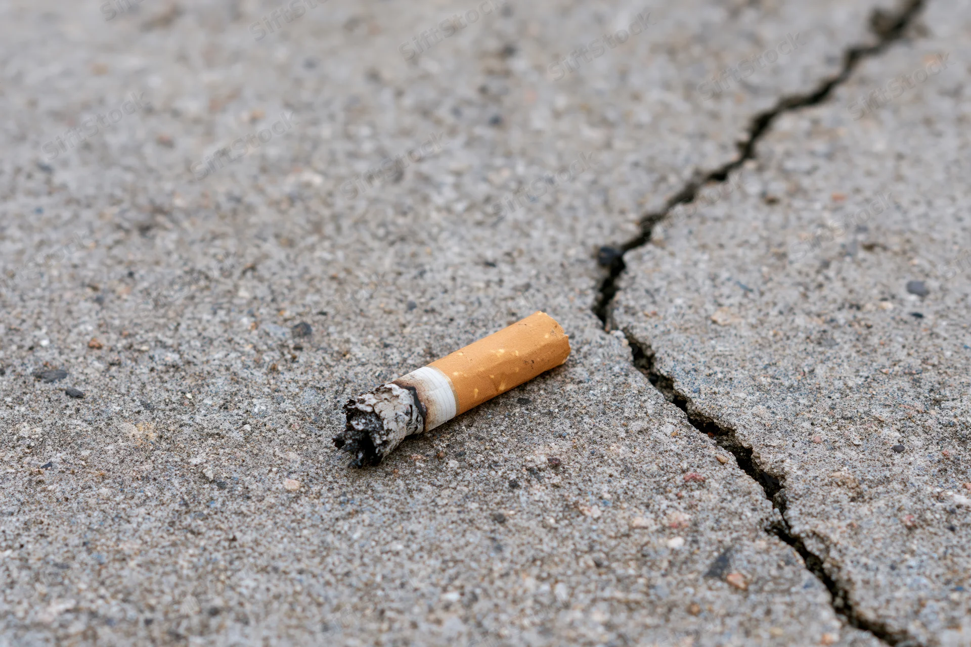 Extinguished cigarette butt lying on cracked concrete pavement