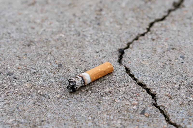 Extinguished cigarette butt lying on cracked concrete pavement