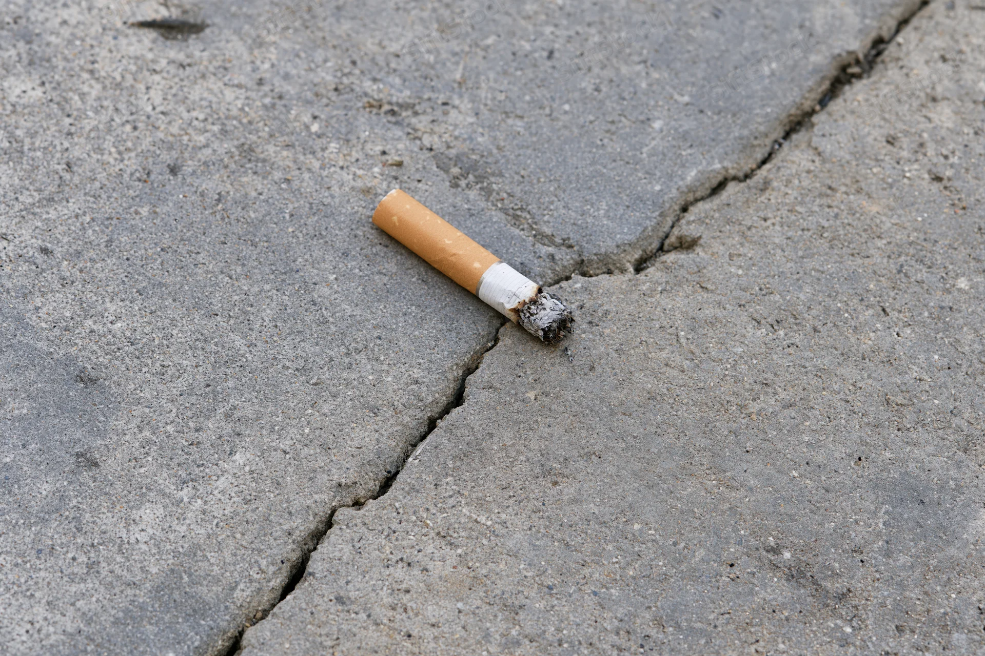 Extinguished cigarette butt lying on cracked concrete pavement