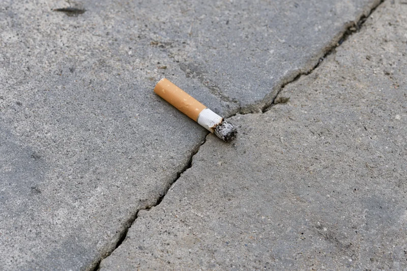 Extinguished cigarette butt lying on cracked concrete pavement