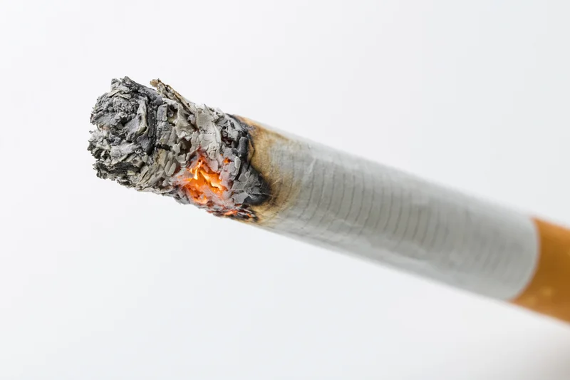 Lit cigarette angled diagonally with burning tip and ash against white background