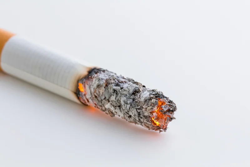 Lit cigarette angled diagonally with burning tip and ash on white background