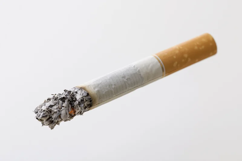 Lit cigarette with glowing ember and crumbling ash on white background