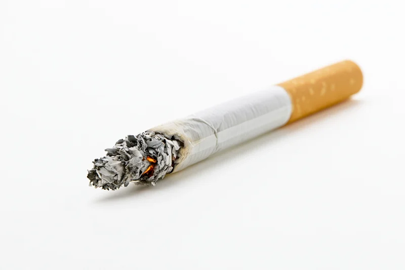 Lit cigarette with glowing ember and ash on white background