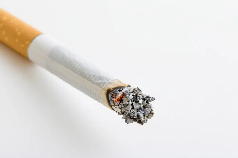 Lit cigarette with glowing ember and ash on white background