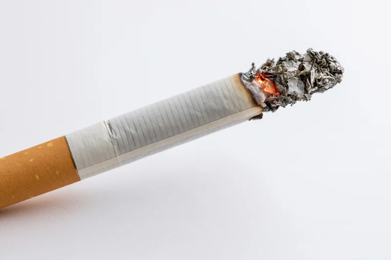 Lit cigarette with glowing ember and ash on white background