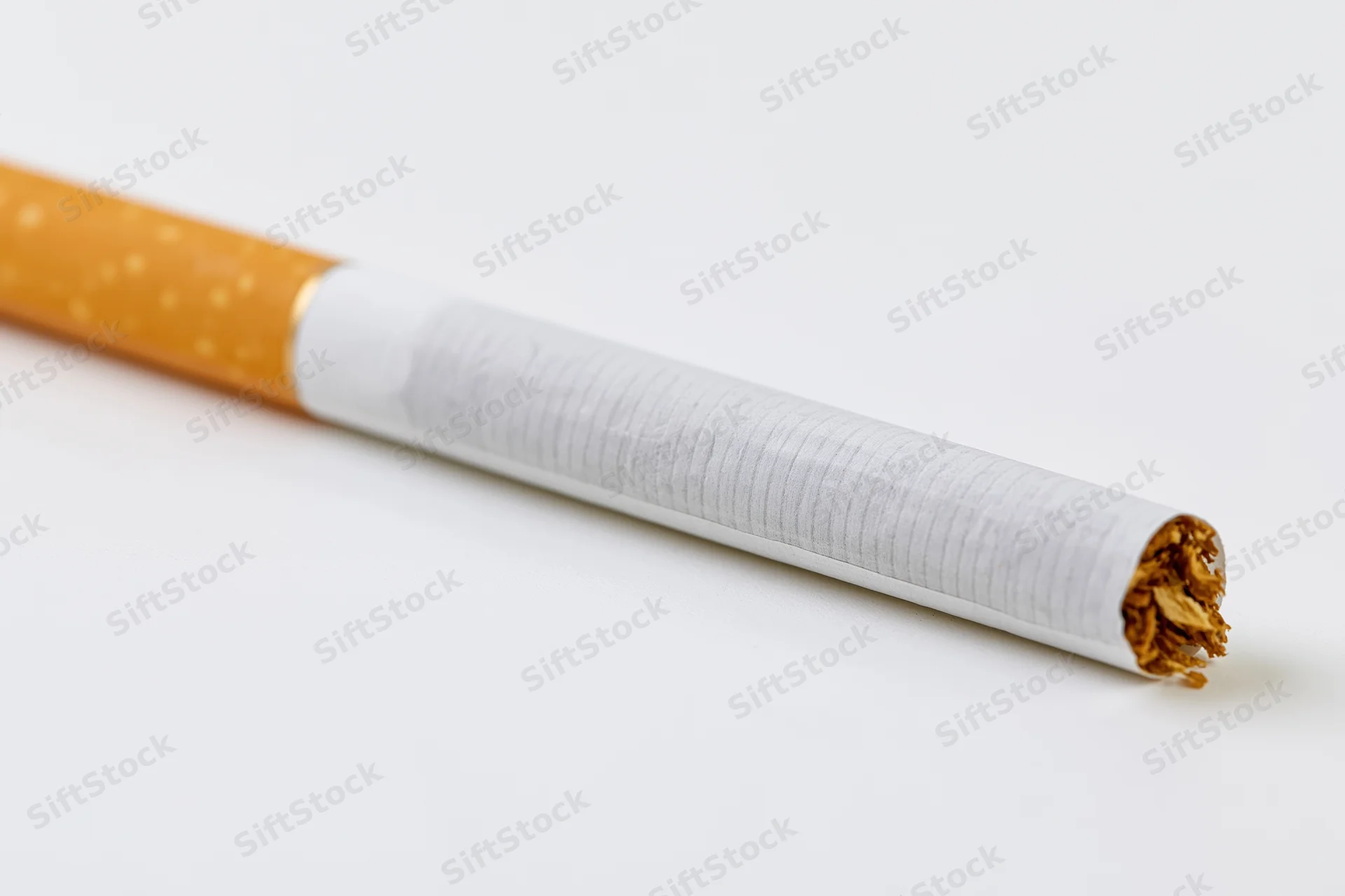 Unlit cigarette lying diagonally on white background with visible tobacco and filter
