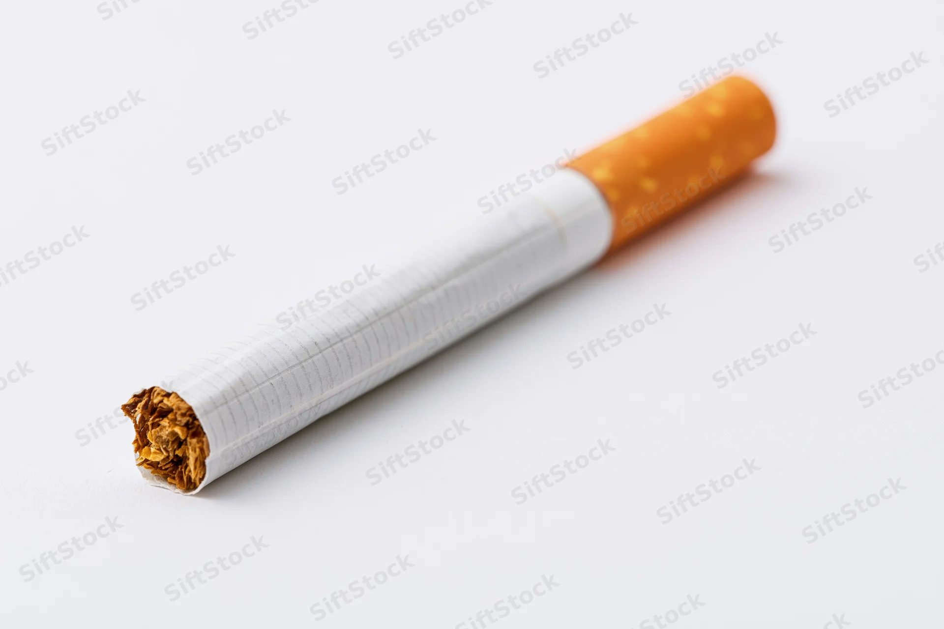 Unlit cigarette with orange filter lying diagonally on white background
