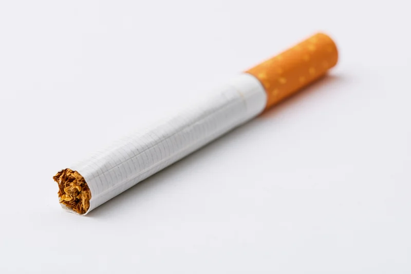 Unlit cigarette with orange filter lying diagonally on white background