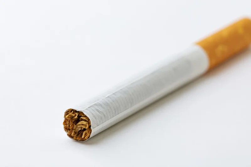 Unlit cigarette lying diagonally on white background with visible tobacco and filter