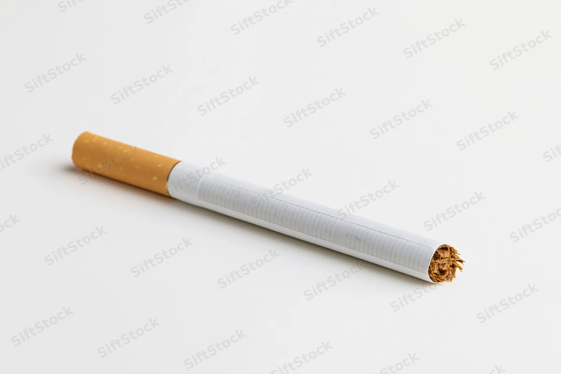 Unlit cigarette with white paper body and brown filter lying diagonally on white background