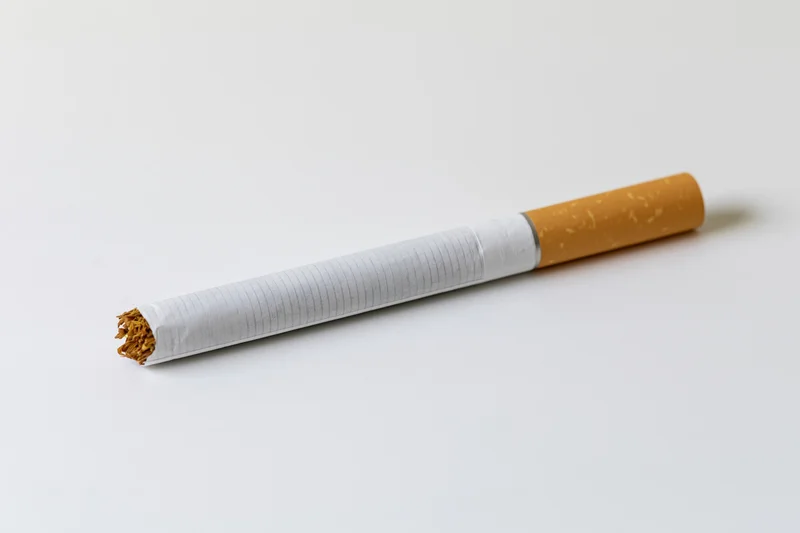 Unlit cigarette with white paper body and brown filter lying diagonally on white surface