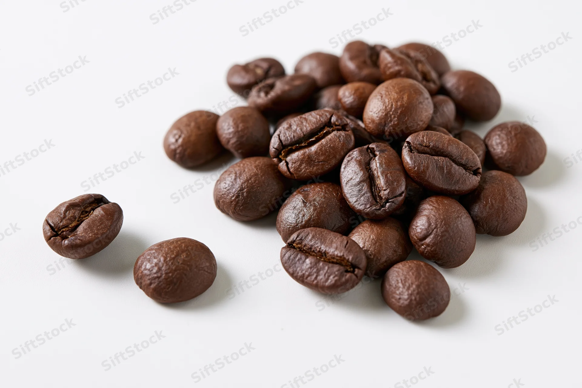 Roasted coffee beans scattered loosely on a white surface