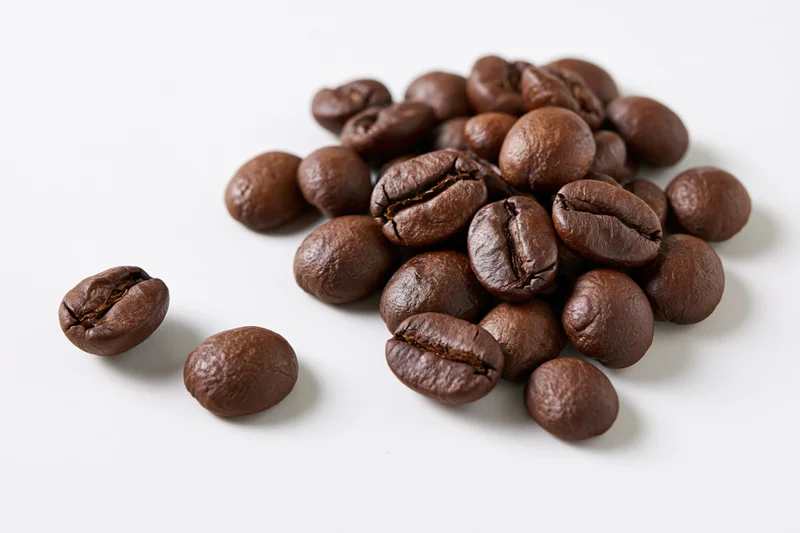Roasted coffee beans scattered loosely on a white surface