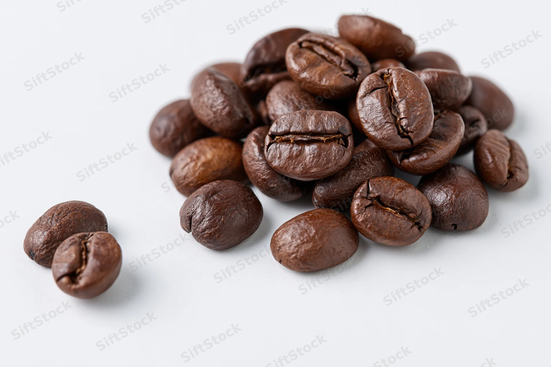 Roasted coffee beans scattered in a small pile on a white surface