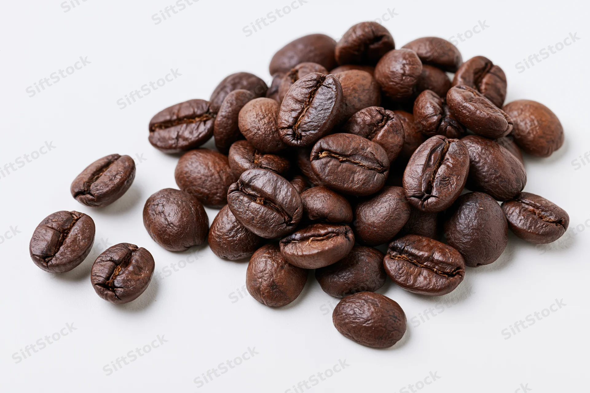 Roasted coffee beans scattered in a loose pile on a white background